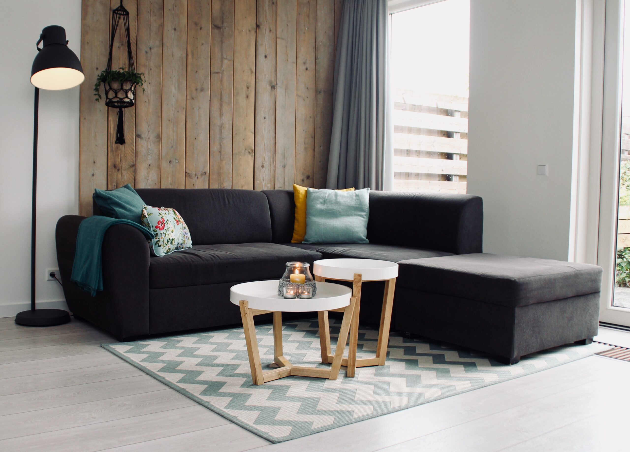 Black sectional couch with teal pillows in a living room with a wooden wall